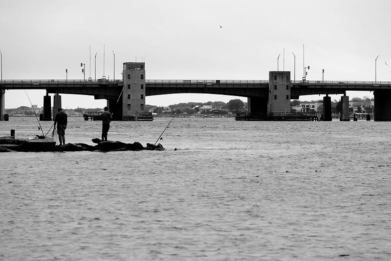 Drawbridge towers across a flat estuary in black and white