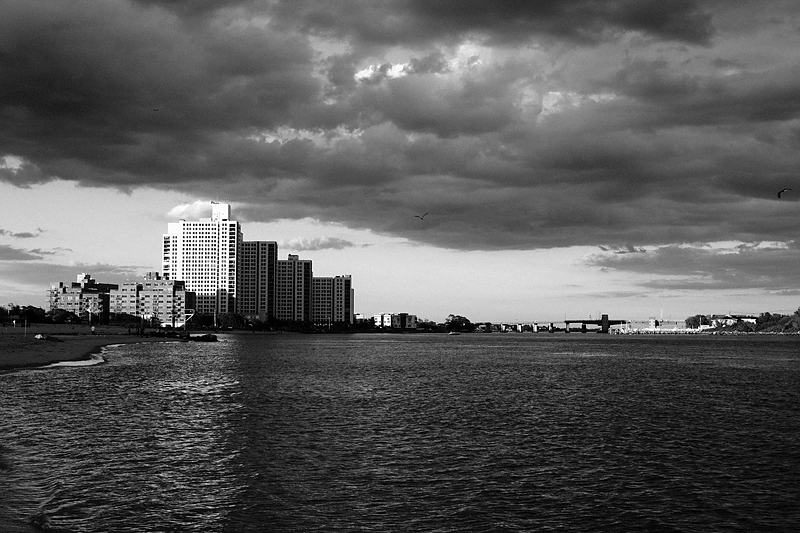 Waterfront apartment blocks under a heavy grey sky, black and white