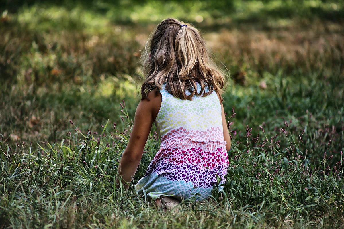 Young girl sitting in long grass, backlit, the background thrown well out of focus