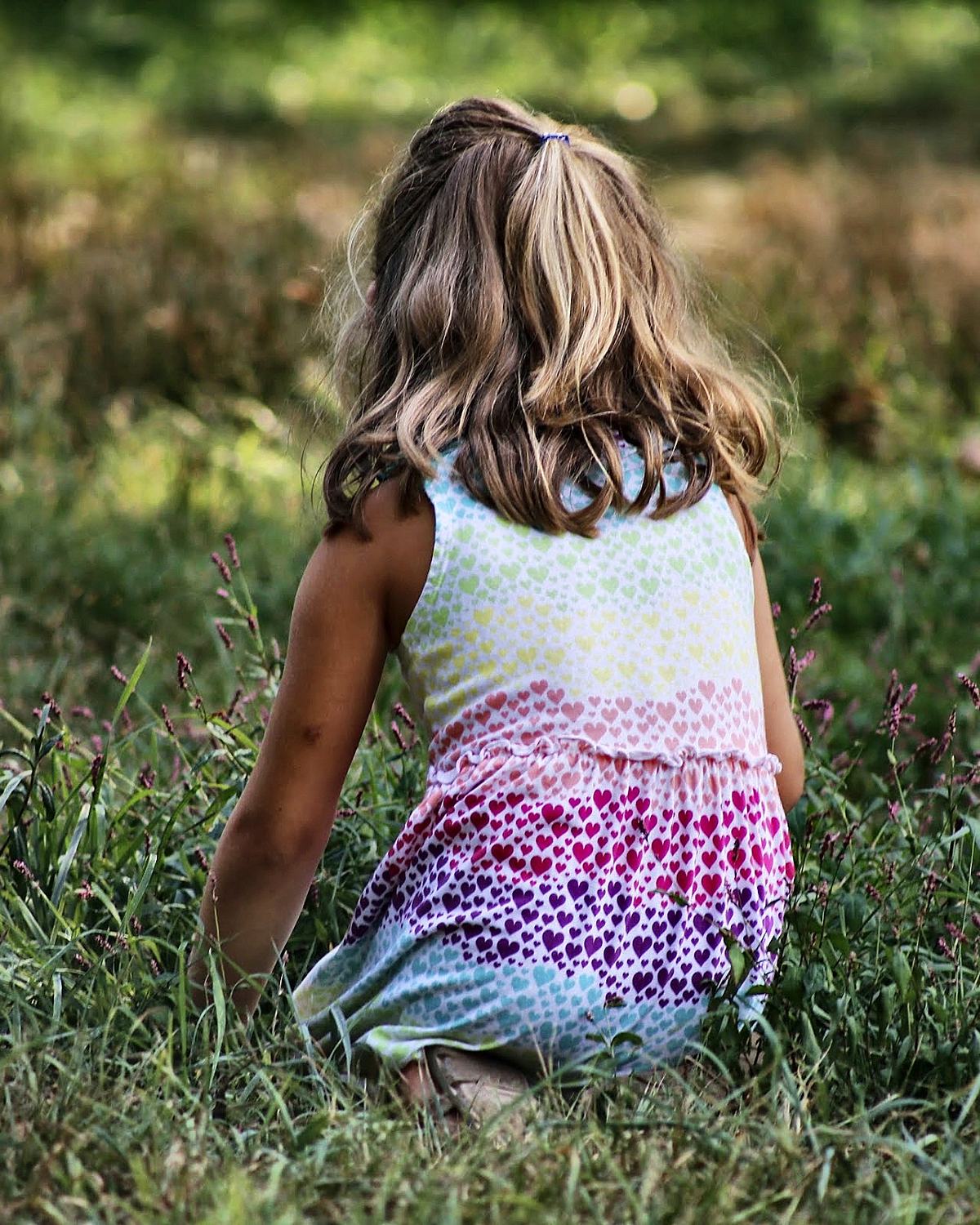 Young girl sitting in long grass, backlit in late afternoon