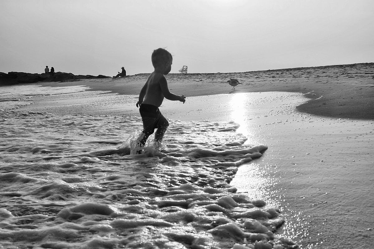 Child running through shallow surf, backlit and in monochrome