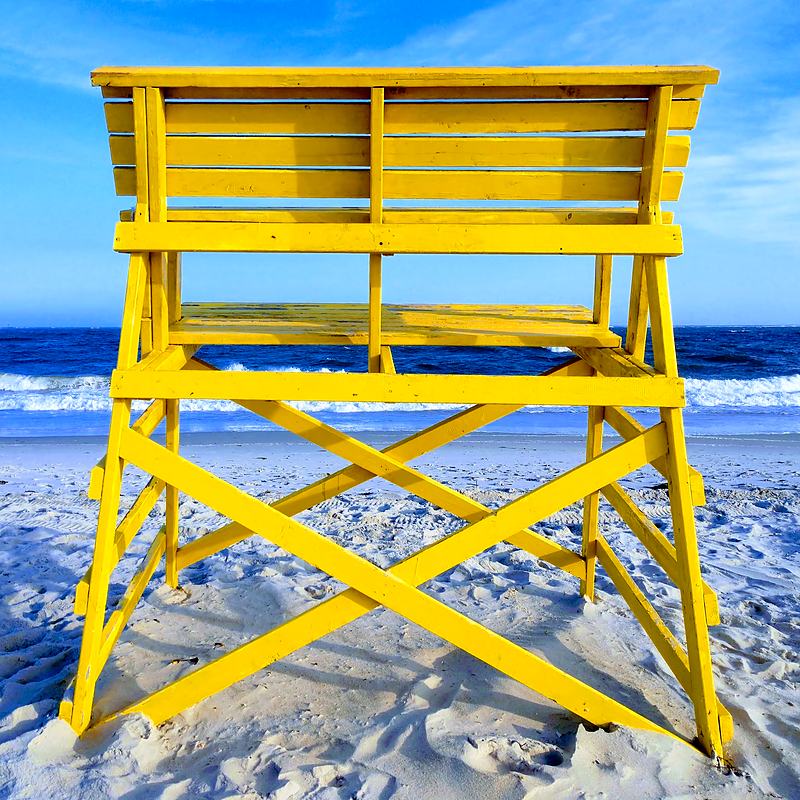 Yellow lifeguard chair standing against a flat blue sea
