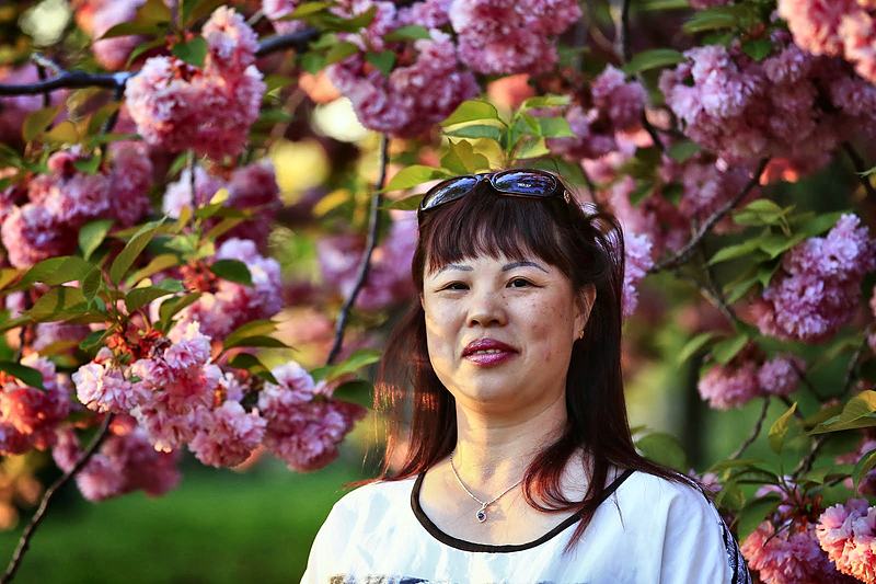 Woman framed by pink blossom, looking past the camera