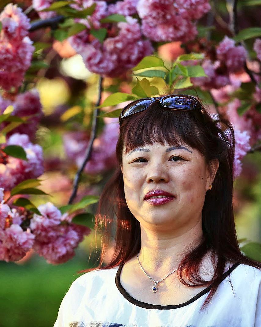 Woman framed by pink blossom, looking past the camera