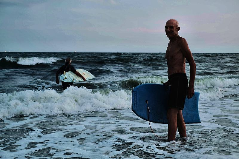 Bodyboarder walking out of the water as another rider takes a wave