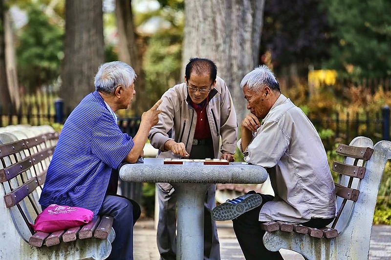 Three men bent over a stone chess table in a park