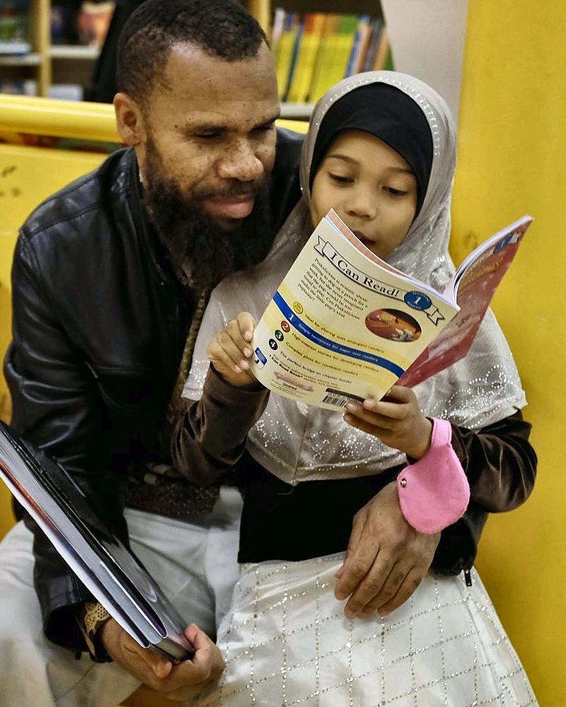 A man and a child reading together against a bright yellow wall