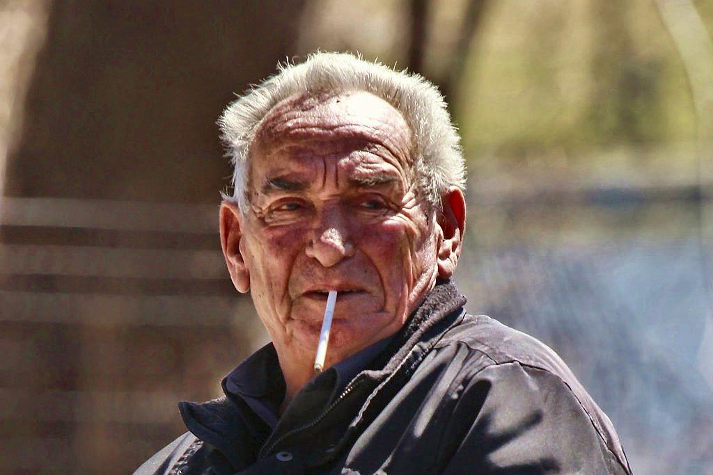Older man outdoors, cigarette in his lips, weathered face filling the frame