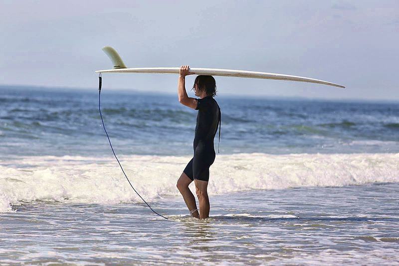 Surfer wading out through the shallows carrying a board overhead