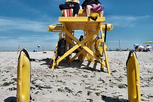 Two lifeguards on a yellow beach tower, rescue buoys planted in the sand