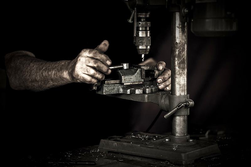 Reference frame: hands operating a pillar drill in a dark workshop