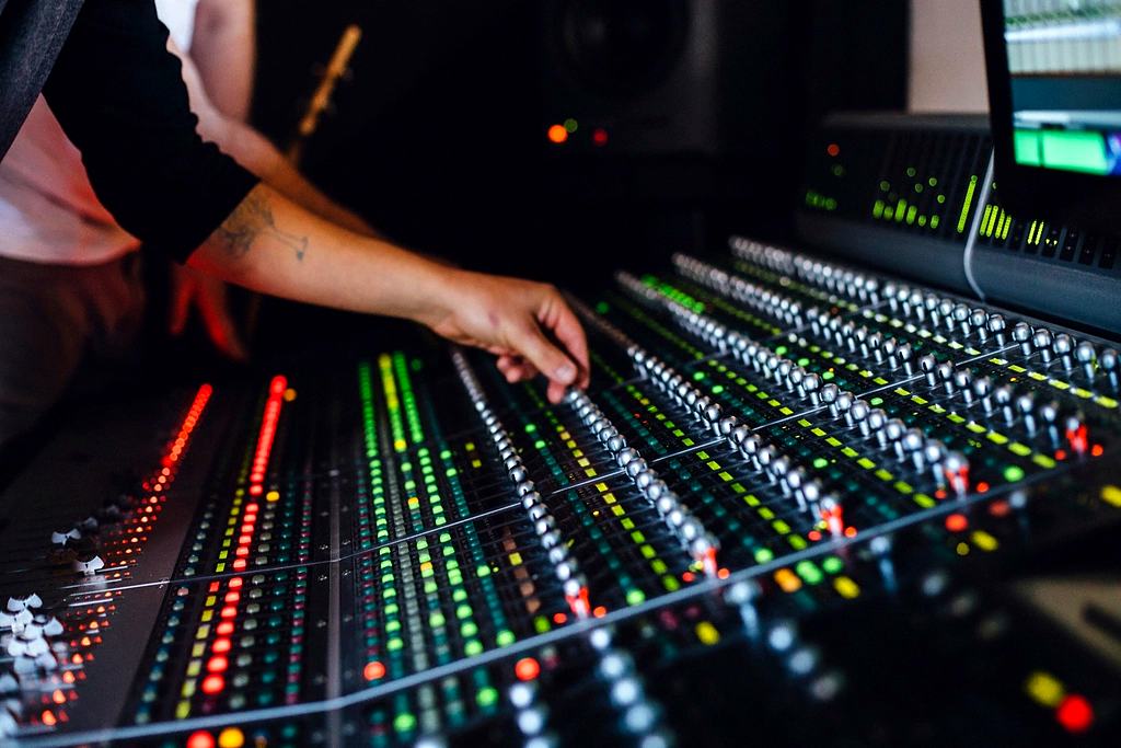 Reference frame: hands riding the faders on a lit mixing console