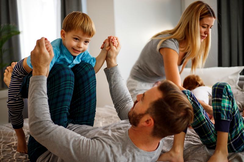 Reference frame: parents playing with a toddler on the bed in morning light