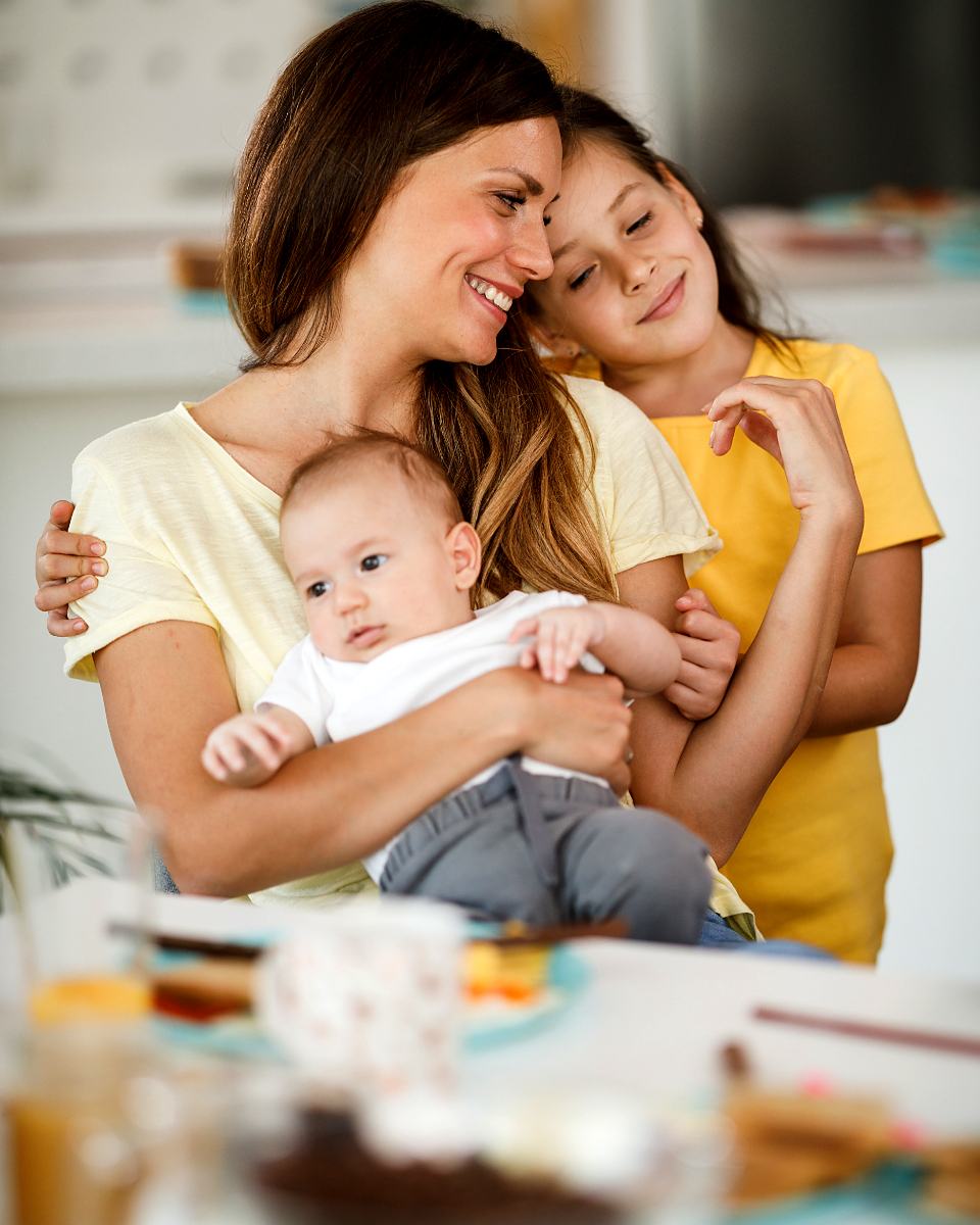 Reference frame: a mother holding a newborn with her older child alongside
