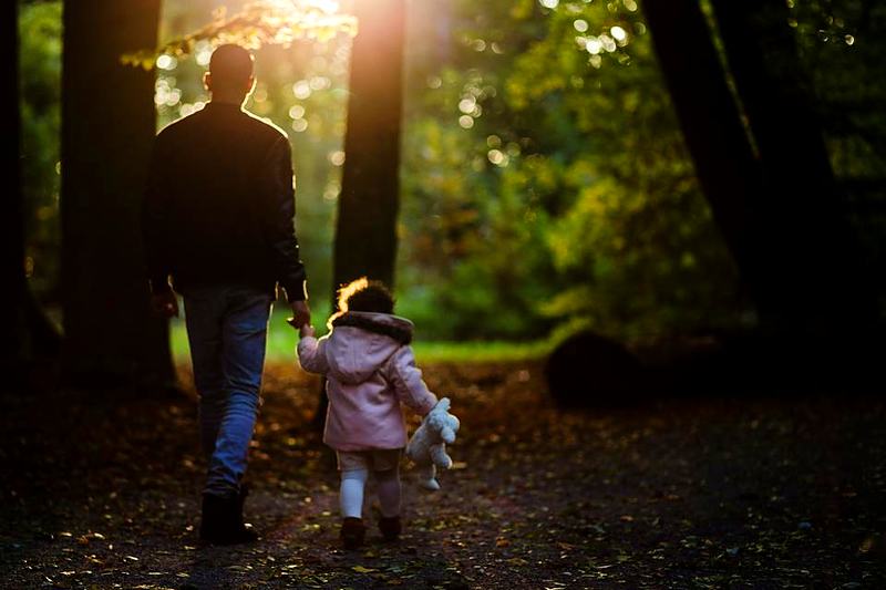 Reference frame: a parent and a small child walking a woodland path, backlit