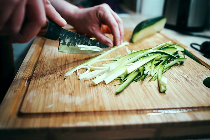 Reference frame: hands slicing vegetables thinly on a wooden board