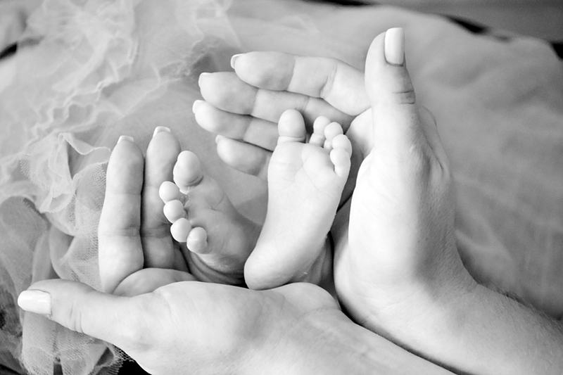 Reference frame: newborn feet cupped in a pair of adult hands, in monochrome
