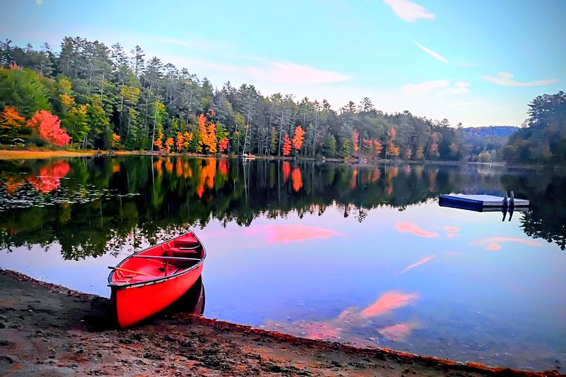 Red canoe drawn up on an autumn lake shore